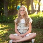 girl with blue bow in hair smiles and sits in sunny grass in Tennessee