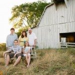 Family sitting on old bench and smiling by barn in sunny field in Tennessee