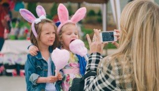 Blonde mother takes picture on smart phone of two young children in bunny ears eating cotton candy at holiday event in Nashville Tennessee