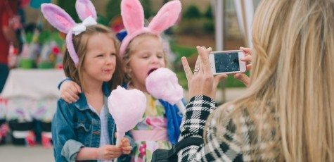 Blonde mother takes picture on smart phone of two young children in bunny ears eating cotton candy at holiday event in Nashville Tennessee