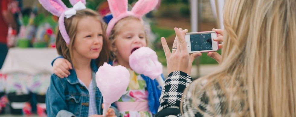 Blonde mother takes picture on smart phone of two young children in bunny ears eating cotton candy at holiday event in Nashville Tennessee