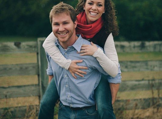 Couple smile and embrace by wooden fence for wedding engagement session in Tennessee