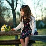 Child in flower dress sits on old fence and holds flowers in Tennessee