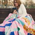 mother and daughter sit on bench outside under a blanket and smile in Tennessee