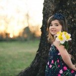 child in flower dress holds flowers by tree in Tennessee