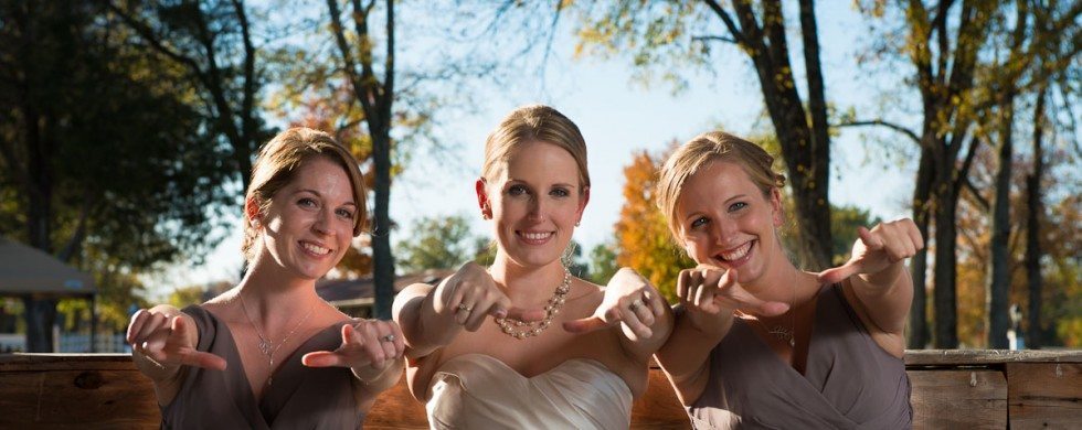 Bride and bridesmaids smile and point on wooden bench outside at wedding in Lebanon Tennessee
