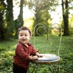 Smiling child leans on chair in green grass for family portrait in Nashville Tennessee