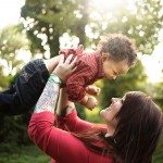 Smiling mother holds smiling baby in the air for family portrait in green field in Nashville Tennessee