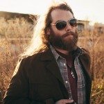 Band member in glasses stand in amber field for portrait in Nashville Tennessee