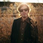 Band member in glasses stands in amber field for portrait in Nashville Tennessee