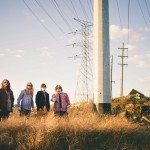 Band members in amber grass field stand next power lines for portrait in Nashville Tennessee