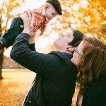 Father holds baby in the air and mother smiles in autumn landscape for family portrait in Nashville Tennessee