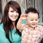 Mother smiles and holds baby by wooden door for portrait in Nashville Tennessee