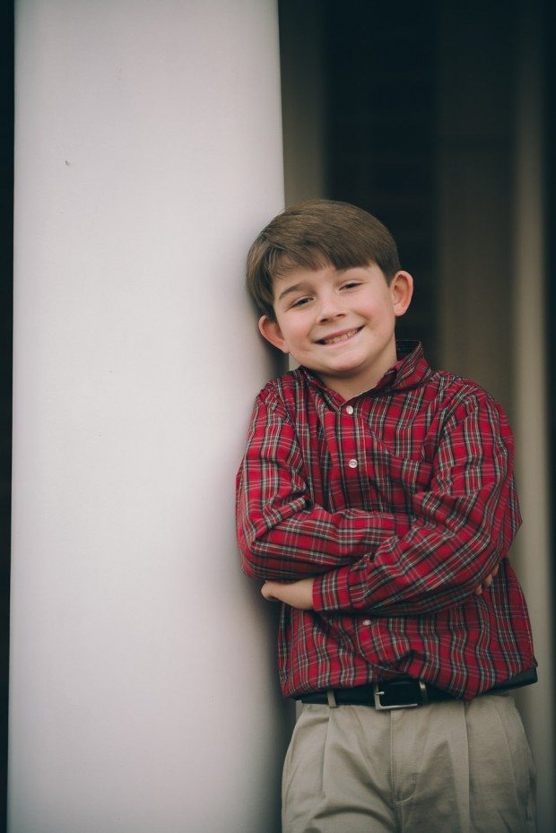 Child in red shirt leans on white column outside house in Tennessee