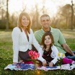smiling young family sit outside on blanket with flowers in Tennessee